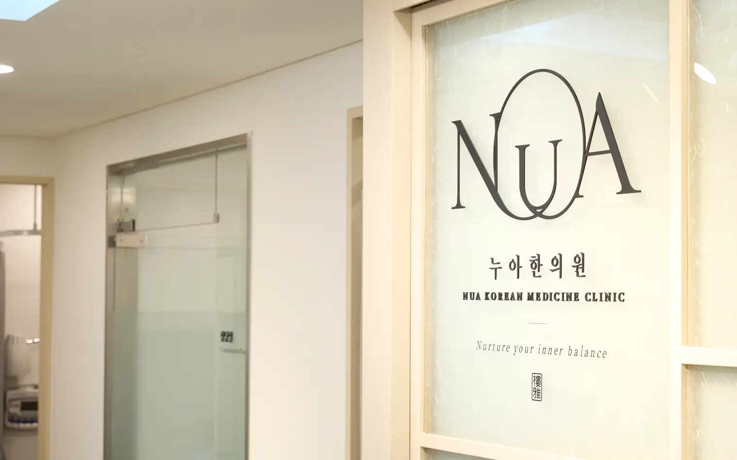 NuA Korean Medicine Clinic logo on a glass wall engraved with the words 'Nurture your inner balance'