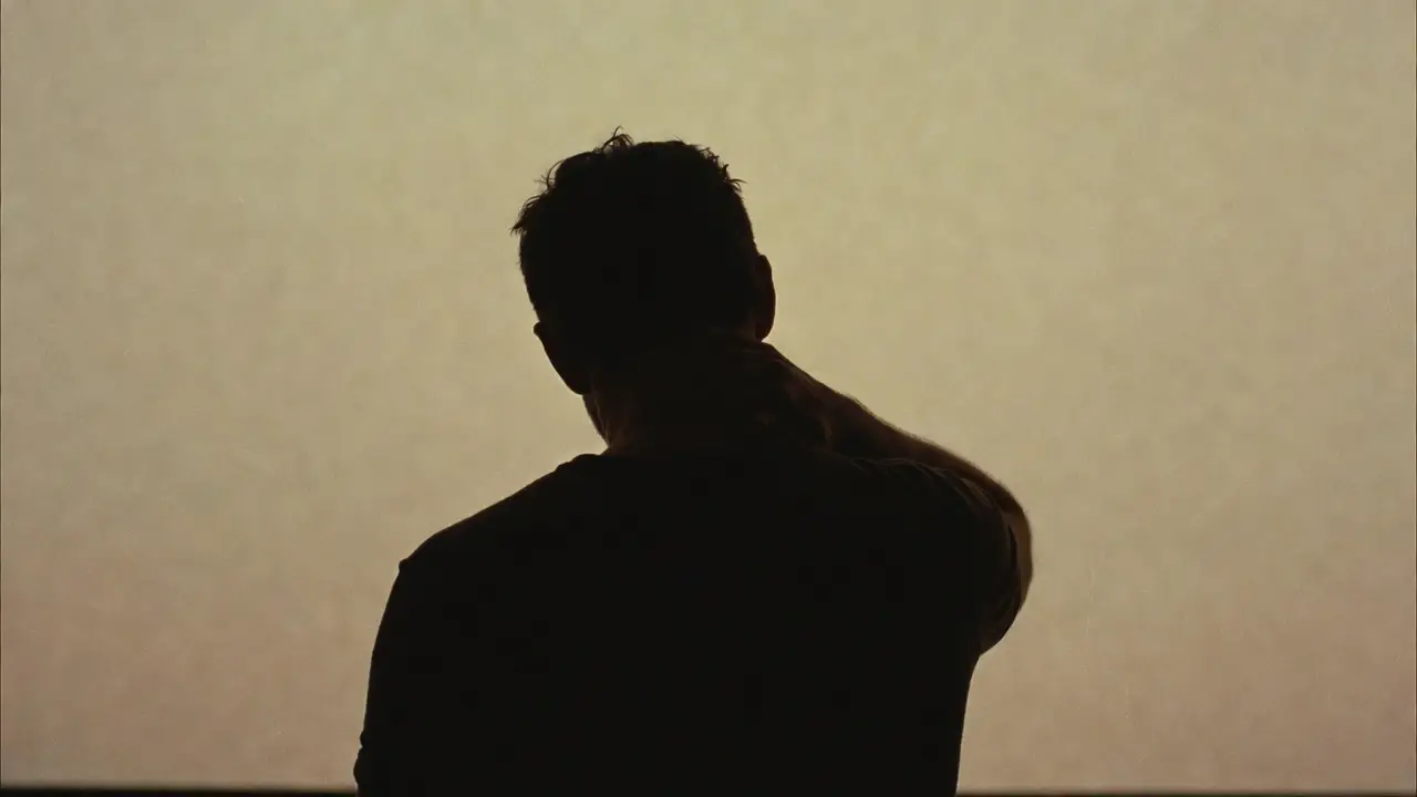 Silhouette from behind of a person with a hunched posture holding the back of the neck