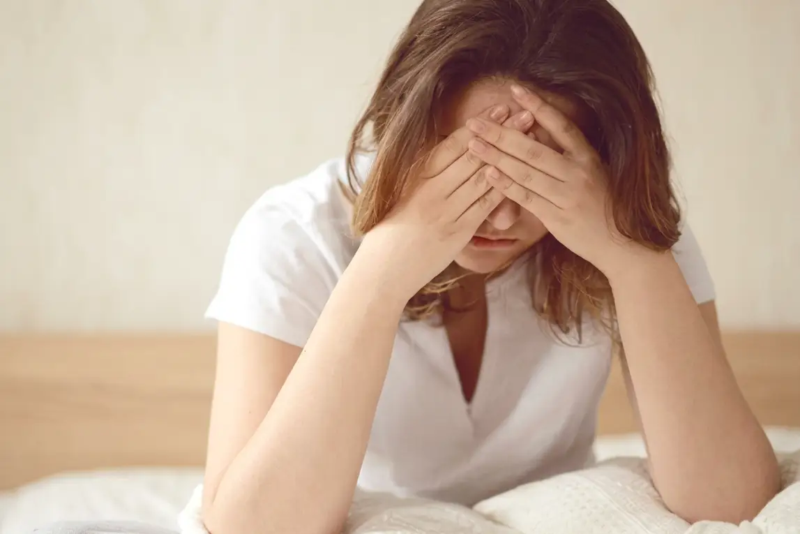 A woman sitting on a bed with her face in both hands