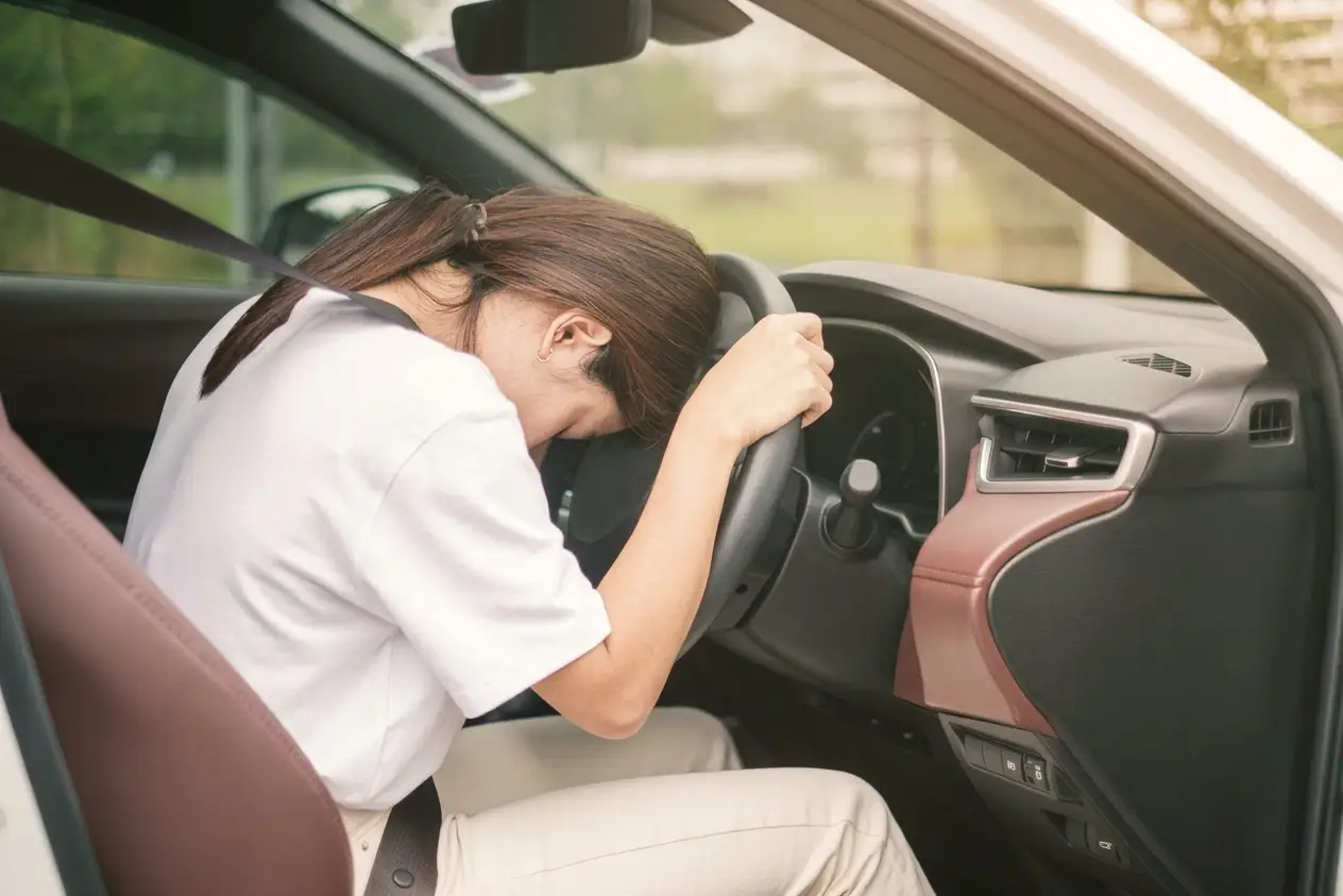 A woman sitting still with her forehead resting on the steering wheel