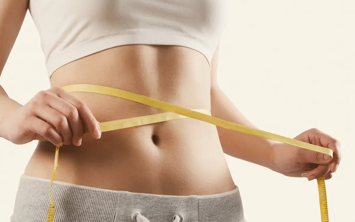 A woman measuring her waist with a tape measure